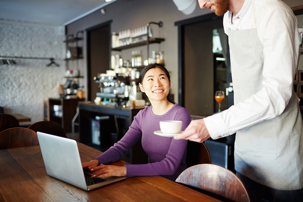 Woman working on laptop in cafe being served coffee